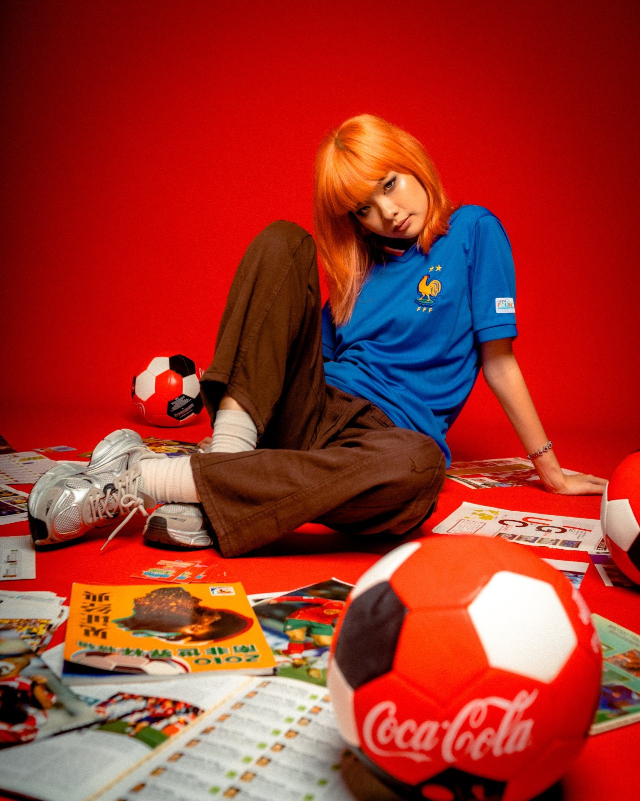 Editorial campaign, red backdrop, seated with footballs