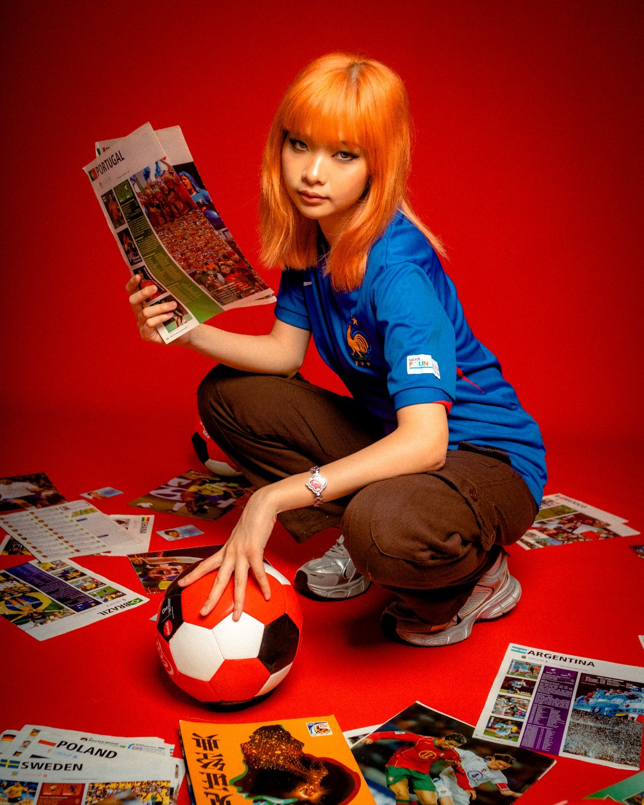 Editorial campaign, red backdrop, crouching with magazine and football