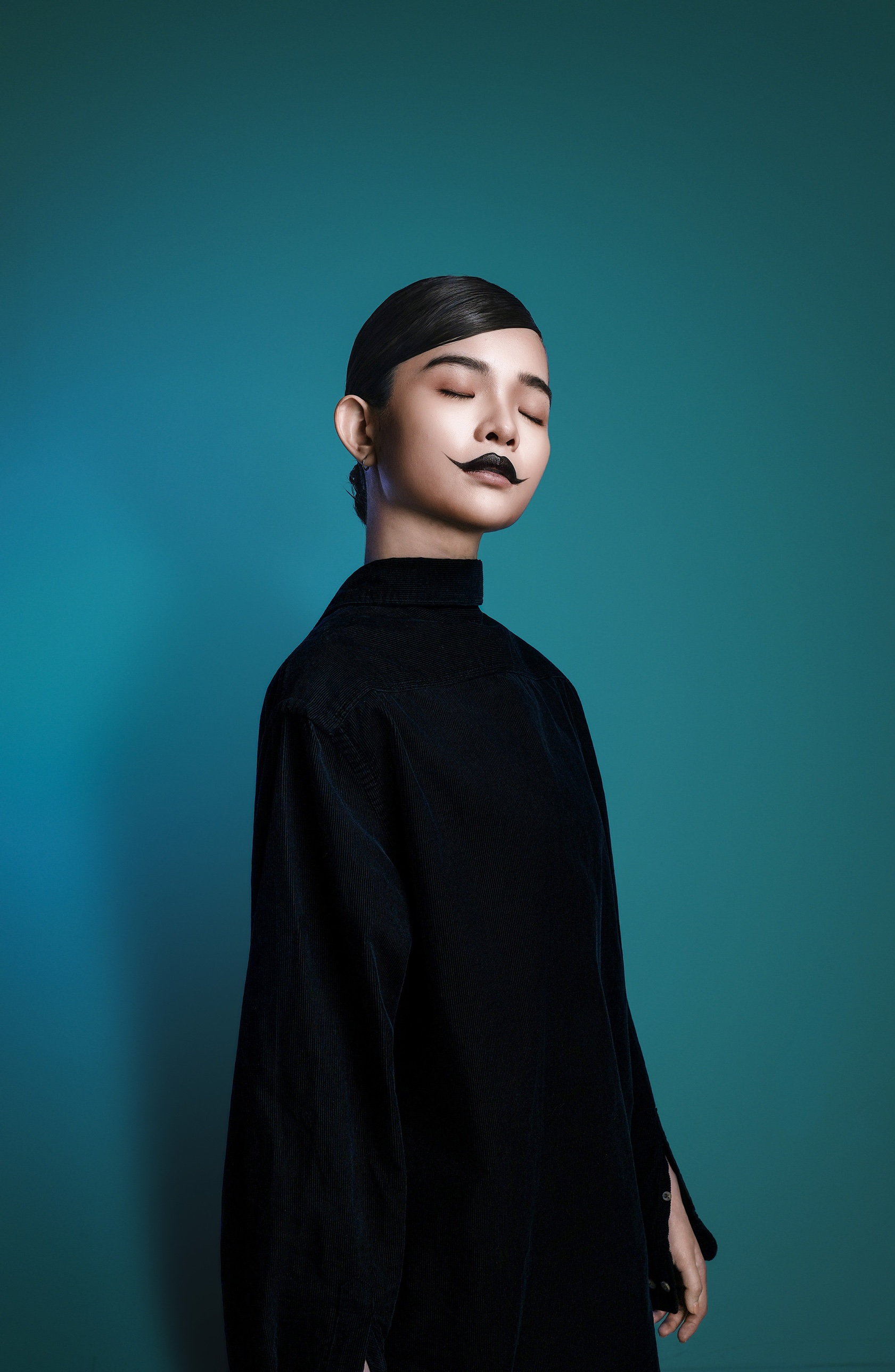 Eyes closed with a painted moustache, teal backdrop