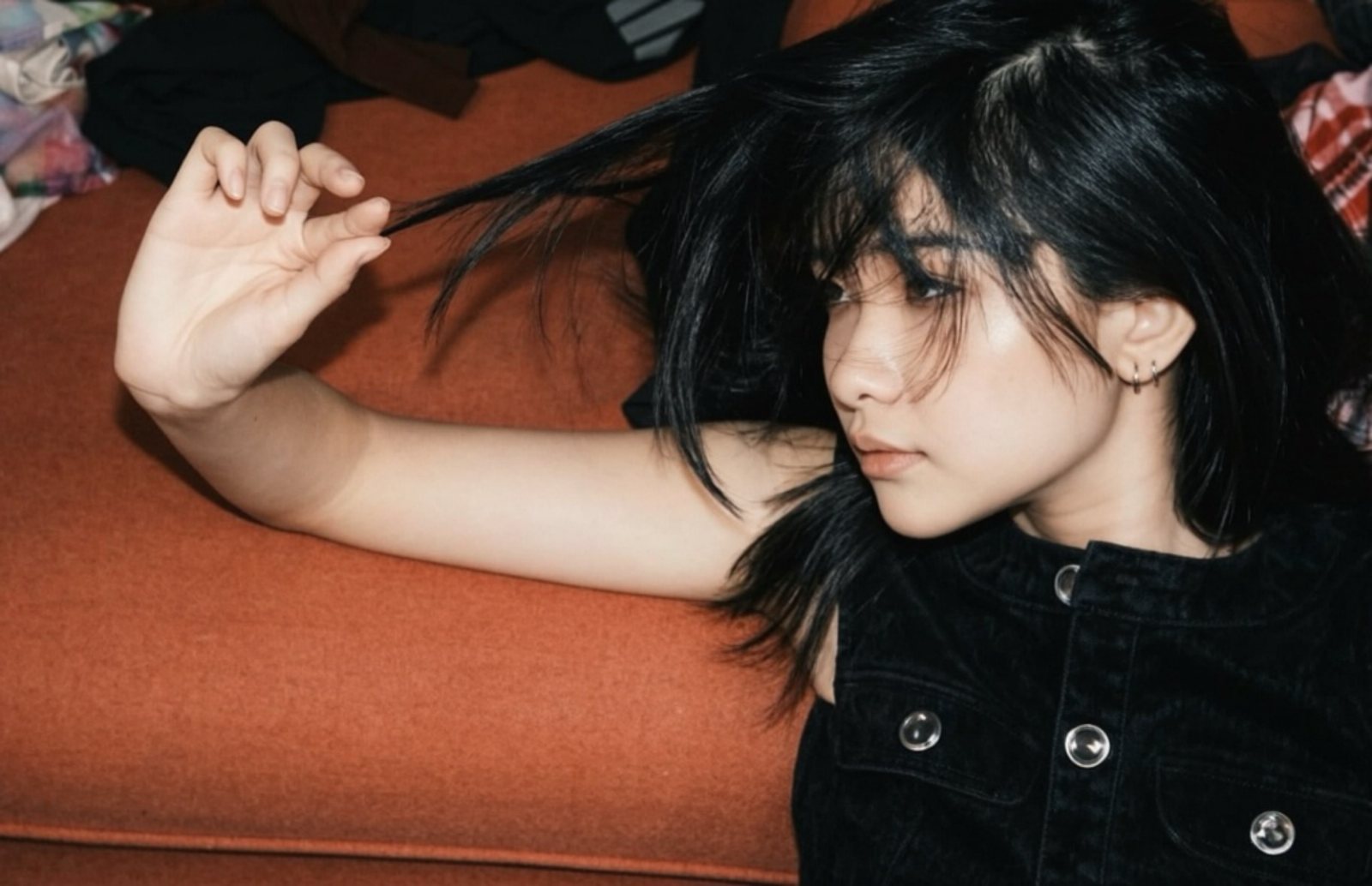 Lying on an orange sofa, twisting a strand of hair