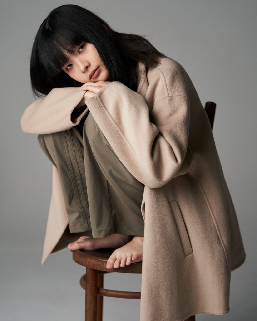 Studio portrait, camel coat, crouched on stool